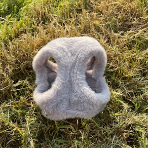 May include: A gray faux fur dog harness with a silver metal ring.