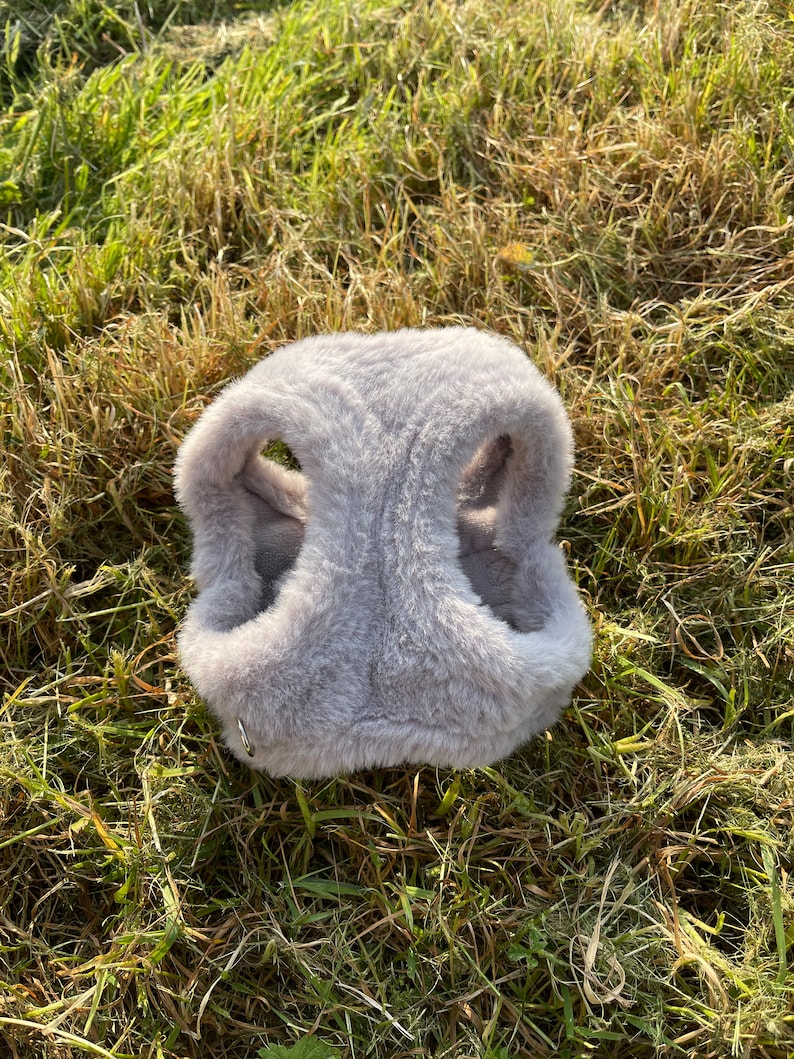 May include: A gray faux fur dog harness with a silver metal ring.