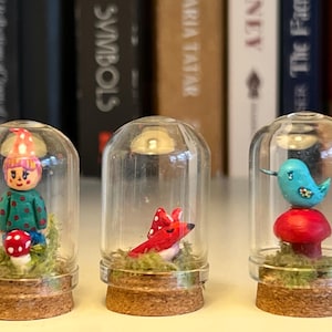 以下が含まれることがあります： コルクベースのミニチュアガラスドーム3つ。それぞれに風変わりなフィギュアが入っています。1つは赤い水玉模様のキノコを持つノーム、もう1つは赤いキツネ、最後は赤いキノコの上にいる青い鳥です。背景には本棚があります。