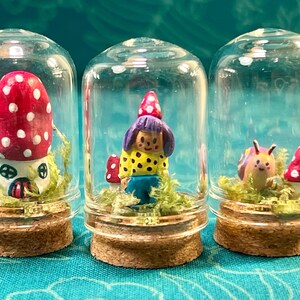 以下が含まれることがあります： 3つのミニチュアテラリウム。それぞれガラスドームの中に、キノコの家、ノーム、カタツムリが緑の苔の上に配置されています。キノコの傘は赤色で白い水玉模様です。