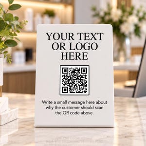 May include: A white rectangular sign featuring the black text YOUR TEXT OR LOGO HERE, a central QR code, and the additional black text Write a small message here about why the customer should scan the QR code above.