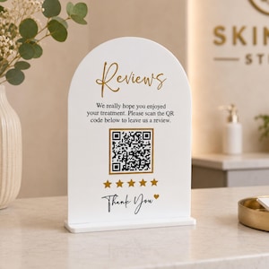 Pode incluir: Uma placa branca em forma de arco com texto em dourado e preto que diz Reviews, We really hope you enjoyed your treatment. Please scan the QR code below to leave us a review., um código QR, cinco estrelas douradas e Thank You com coração.