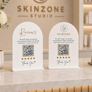 May include: Two white arched acrylic signs with gold text and graphics. The left sign reads Reviews, and the right sign features the Skinzone Studio logo. Both include a QR code, five gold stars, and the text We really hope you enjoyed your treatment.