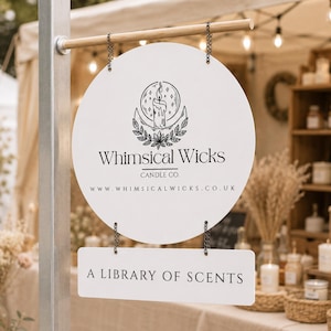 Könnte beinhalten: Ein weißes, rundes Schild, das an zwei Ketten an einer Holzstange hängt, mit einem schwarzen Kerzenlogo und dem Text Whimsical Wicks Candle Co. sowie www.whimsicalwicks.co.uk. Darunter befindet sich ein rechteckiges weißes Schild mit der Aufschrift A LIBRARY OF SCENTS.