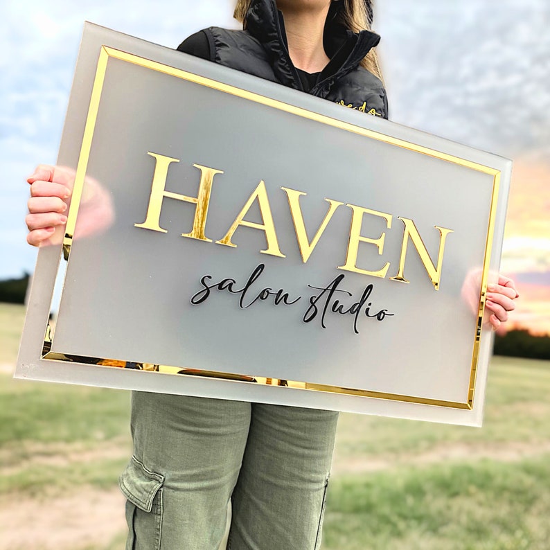 May include: A frosted glass sign with a gold frame and the text "HAVEN salon studio" in black and gold lettering.