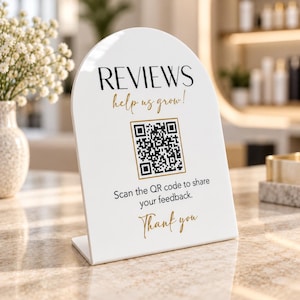 Könnte beinhalten: Ein bogenförmiges weißes Acrylschild mit dem schwarzen Text REVIEWS, dem goldenen Schriftzug help us grow!, einem zentralen schwarz-weißen QR-Code in einem goldenen Rahmen, dem schwarzen Text Scan the QR code to share your feedback. und Thank you in Gold.