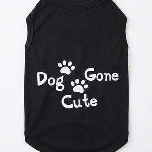 Op de afbeelding: Zwart hondenhemd met witte tekst en pootafdrukken. De tekst luidt "Dog Gone Cute". De mouwloze top is gemaakt van een zacht materiaal en heeft een afgeronde zoom.