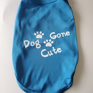 Op de afbeelding: Een blauw honden-T-shirt met de witte tekst "Dog Gone Cute" en pootafdrukken. Het shirt is gemaakt van een zacht materiaal en is ontworpen voor een hond.