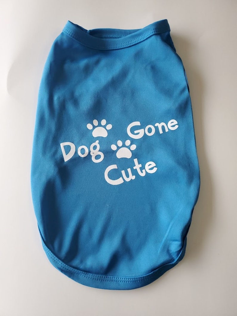 Op de afbeelding: Een blauw honden-T-shirt met de witte tekst "Dog Gone Cute" en pootafdrukken. Het shirt is gemaakt van een zacht materiaal en is ontworpen voor een hond.