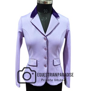 Pode incluir: Casaco de equitação lilás com gola e acabamentos em veludo roxo escuro. O casaco tem um corte sob medida, três botões e dois bolsos frontais. O texto "EQUESTRIAN PARADISE Private limited" está impresso no canto inferior esquerdo.