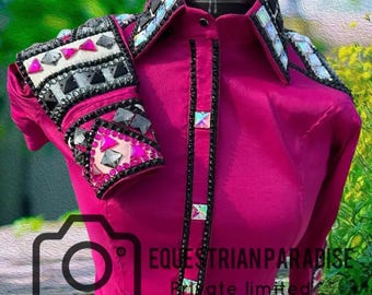 May include: A magenta equestrian show shirt with black and crystal accents. The shirt features decorative embellishments on the collar, shoulders, and cuffs. The text "EQUESTRIAN PARADISE" is visible on the lower right side of the shirt.