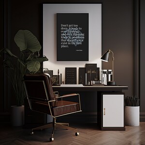 Puede incluir: Una oficina en casa con un escritorio marrón oscuro, una lámpara negra, libros y artículos de papelería. Un póster negro enmarcado con texto blanco cuelga sobre el escritorio. Una silla de cuero marrón con detalles dorados está frente al escritorio. Una planta en maceta está a la izquierda.