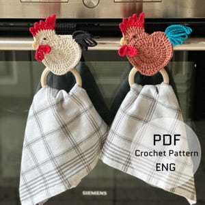 May include: Two crochet chicken kitchen towel holders with wooden rings and plaid towels. One chicken is cream-coloured with a red comb and wattle, the other is brown with a red comb and blue tail. The towels are grey and white.