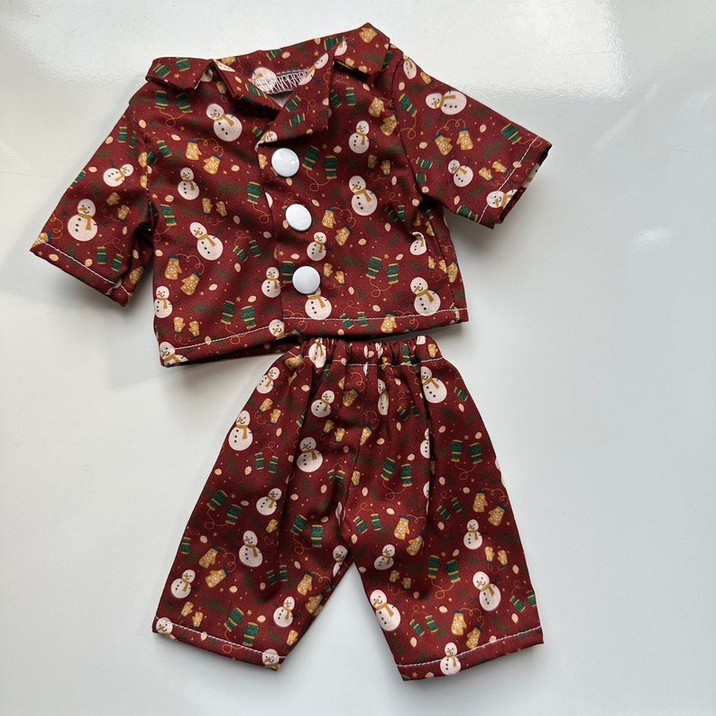Puede incluir: Un conjunto de pijama rojo y blanco con un patr&oacute;n de mu&ntilde;eco de nieve y guantes. El conjunto incluye una camisa de manga larga con cuello abotonado y pantalones a juego.