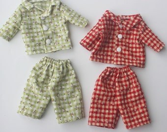 Puede incluir: Dos conjuntos de pijamas para muñecas. Un conjunto es verde con estampado de cuadros blancos y flores. El otro conjunto es rojo con estampado de cuadros blancos y flores.