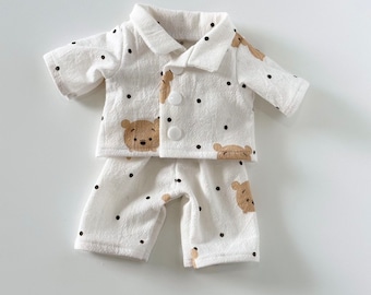 May include: White pyjamas with a brown bear print and black polka dots. The pyjamas have a button-up top with short sleeves and matching trousers.