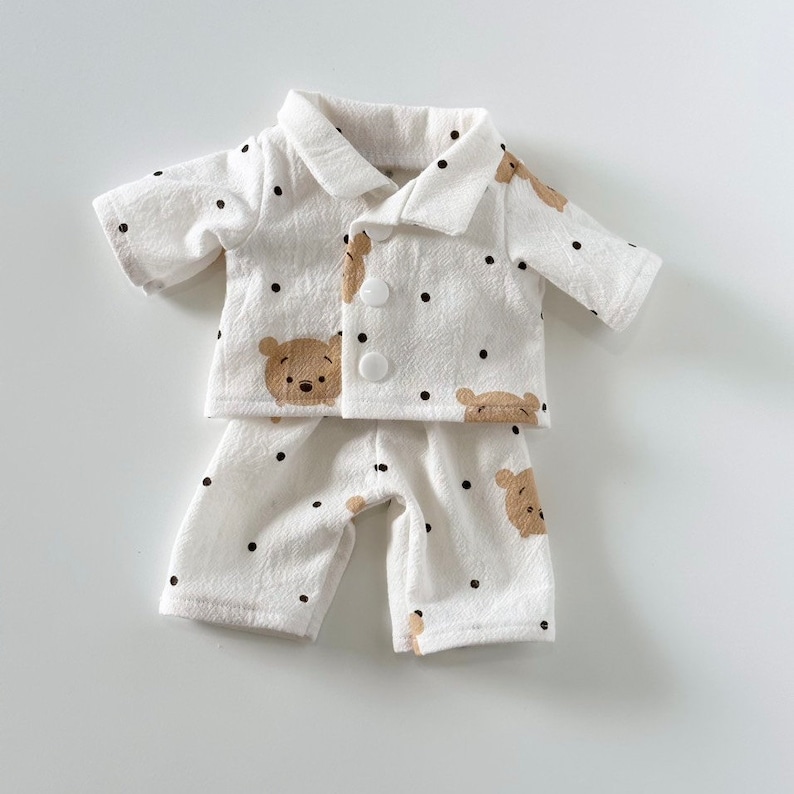 Puede incluir: Pijama blanco con estampado de oso marr&oacute;n y lunares negros. El pijama tiene una parte superior abotonada con mangas cortas y pantalones a juego.