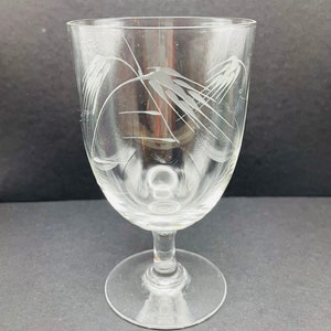May include: A clear glass goblet with a stem and a wide base. The goblet has an etched design of wheat stalks.