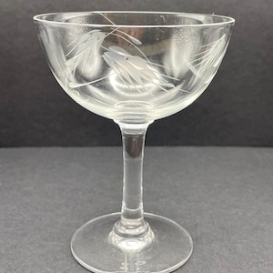 May include: A clear glass stemmed champagne coupe with a delicate etched design of wheat stalks.