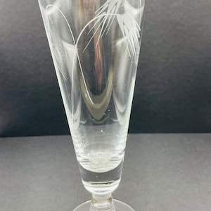 May include: A clear glass beer glass with a tall, slender stem and a wide base. The glass has an etched design of wheat stalks on the side.
