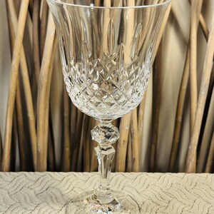 May include: A clear crystal wine glass with a diamond-cut pattern on the bowl and a faceted stem. The glass has a wide bowl and a round base. The background features vertical brown bamboo stalks.