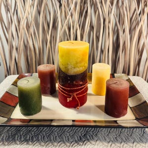 May include: Five candles on a decorative tray. The candles are in various colors, including red, green, yellow, and brown. The tray is made of ceramic and has a colorful design.