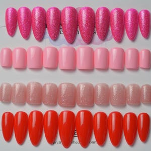 May include: A collection of artificial nails in various shades of pink and red. The top row features glittery, pointed nails, while the second row displays solid pink, square-shaped nails. The third row has glittery, light pink square nails, and the bottom row showcases bright red, pointed nails.