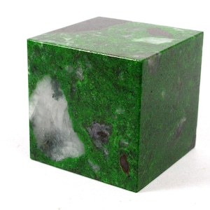 May include: A square, solid block of green stone with white and dark inclusions. The stone has a mossy appearance, with a polished surface. The cube shape is perfect for display or as a decorative element.