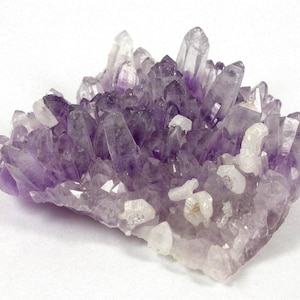 Pode incluir: Um aglomerado de cristais de ametista, exibindo uma gama de tons roxos, do violeta profundo ao lavanda pálido. Os cristais são pontiagudos e agrupados, com alguns detalhes em quartzo transparente.
