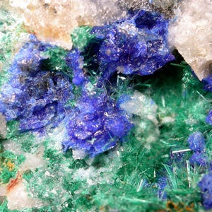 May include: A mineral specimen featuring clusters of deep blue azurite crystals contrasted against vibrant green malachite needles. The geological formation includes translucent white quartz inclusions embedded within the textured, crystalline surface.