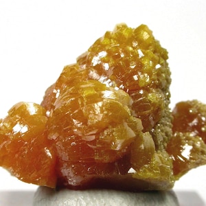 May include: A cluster of vibrant orange wulfenite crystals featuring a complex, multi-faceted structure with a high-gloss, reflective surface. The mineral specimen displays sharp, square-shaped crystal formations that catch the light.