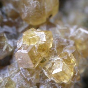 May include: A cluster of translucent, pale yellow mineral crystals with distinct geometric, hexagonal, and multifaceted shapes. The crystalline structure features sharp edges and smooth, reflective surfaces that catch the light, creating a complex, layered arrangement of light-colored, semi-transparent mineral formations.