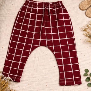 May include: Burgundy and white checkered baby pants. The pants have a grid pattern with white lines on a burgundy background. The pants are made of a soft material and have a comfortable fit.