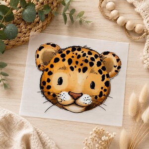 Könnte beinhalten: Ein quadratisches weißes Blatt mit einer zentrierten, stilisierten Illustration eines Leopardenjungen-Kopfes. Der Leopard hat goldgelbes Fell, dunkelbraune Flecken, große schwarze Augen, eine kleine rosa Nase und feine schwarze Schnurrhaare.