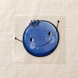 Könnte beinhalten: Ein quadratischer, transparenter Aufkleber mit einer runden, blauen Blaubeerfigur mit lächelndem Gesicht, großen Augen und dünnen, schwarzen, stabartigen Armen, die nach außen ragen. Die Blaubeere hat oben eine dunkelblaue Krone.