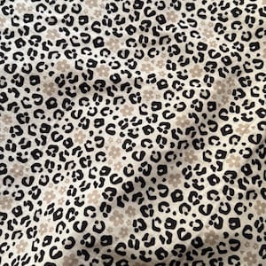 Op de afbeelding: Een crèmekleurige stof met een herhaald patroon van zwarte luipaardvlekken en kleine beige bloemen. De stof heeft een licht gekreukte textuur, wat wijst op een lichtgewicht materiaal.