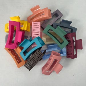 May include: A collection of colorful plastic hair clips in various shapes and sizes. The clips are in shades of pink, blue, green, brown, and yellow.