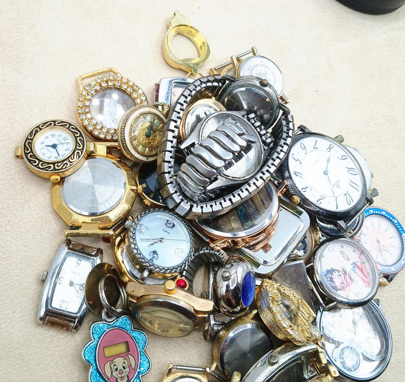 K&ouml;nnte beinhalten: Eine Sammlung verschiedener Armbanduhren und Uhrenteile, darunter diverse runde und rechteckige Geh&auml;use, Metallgliederarmb&auml;nder und Zifferbl&auml;tter mit analogen Anzeigen, teilweise mit dekorativen gold- und silberfarbenen Akzenten.