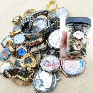 K&ouml;nnte beinhalten: Eine Sammlung verschiedener Vintage-Armbanduhren und Uhrenteile, darunter gold- und silberfarbene Modelle sowie dekorative Zifferbl&auml;tter mit Charakterillustrationen, erg&auml;nzt durch ein Glasgef&auml;&szlig; voller weiterer Uhrenkomponenten.