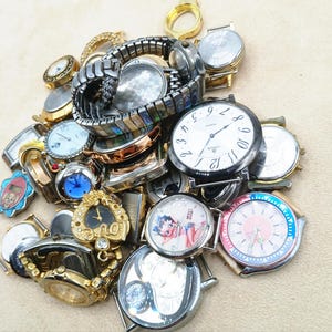K&ouml;nnte beinhalten: Eine gro&szlig;e Sammlung verschiedener Armbanduhren und Uhrenteile in unterschiedlichen Ausf&uuml;hrungen, darunter gold- und silberfarbene T&ouml;ne sowie Metallgliederarmb&auml;nder. Der Haufen enth&auml;lt runde und geformte Zifferbl&auml;tter mit Grafiken.