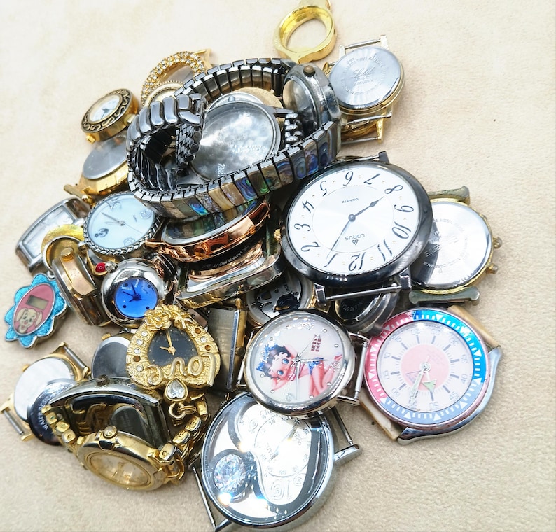K&ouml;nnte beinhalten: Eine gro&szlig;e Sammlung verschiedener Armbanduhren und Uhrenteile in unterschiedlichen Ausf&uuml;hrungen, darunter gold- und silberfarbene T&ouml;ne sowie Metallgliederarmb&auml;nder. Der Haufen enth&auml;lt runde und geformte Zifferbl&auml;tter mit Grafiken.
