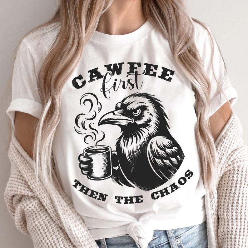 May include: White t-shirt with a black graphic of a raven holding a coffee mug. The text on the shirt reads "CAWFEE first THEN THE CHAOS". The raven is depicted with steam rising from the coffee.