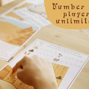 May include: A hand pointing at a game board with a desert theme. The board has a grid with letters and images. The text on the board says "Number of players: unlimited". Several other game sheets are scattered on the wooden surface.