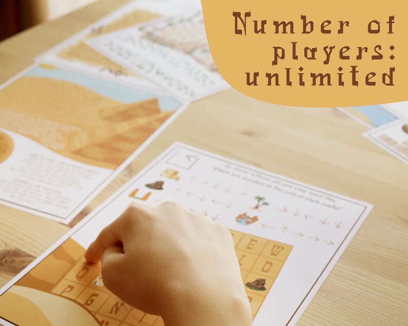 May include: A hand pointing at a game board with a desert theme. The board has a grid with letters and images. The text on the board says "Number of players: unlimited". Several other game sheets are scattered on the wooden surface.