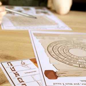 May include: A tabletop scene featuring printed puzzle sheets with circular and rectangular designs. One sheet has a compass-like graphic. A hand holds a pen, suggesting active engagement with the puzzles. The color palette is muted, with beige and brown tones.