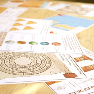 May include: A collection of printed papers with illustrations and text, including a circular design with text and a scroll-like element. The papers feature various graphics and text, with a focus on a tan and brown color scheme. The papers are arranged on a light brown wooden surface.