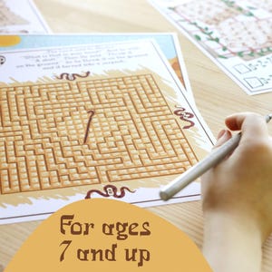 May include: A printed maze puzzle with a brown and tan color scheme. The maze is being traced with a silver pen. The text "For ages 7 and up" is displayed on the bottom of the image. Other printed sheets are in the background.