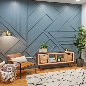 K&ouml;nnte beinhalten: Ein Wohnzimmer mit einer blauen geometrischen Wand, einem braunen Holzregal mit drei geflochtenen K&ouml;rben, einem braunen Ledersessel, einer goldenen Stehlampe und einem wei&szlig;-schwarzen gemusterten Teppich.