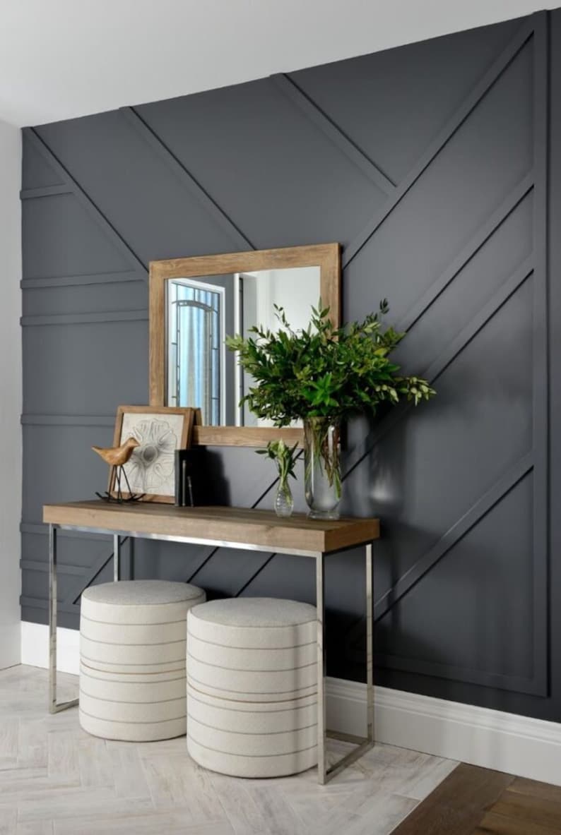 K&ouml;nnte beinhalten: Eine dunkelgraue Wand mit geometrischem Muster, ein Konsolentisch aus Holz mit einem Spiegel dar&uuml;ber und zwei wei&szlig;e Hocker. Der Konsolentisch hat eine Holzplatte und silberne Metallbeine. Der Spiegel hat einen Holzrahmen. Auf dem Tisch stehen Pflanzen in einer Vase.