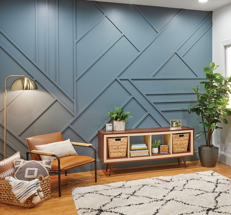 K&ouml;nnte beinhalten: Ein Wohnzimmer mit einer blauen geometrischen Wand, einem braunen Holzregal mit drei geflochtenen K&ouml;rben, einem braunen Ledersessel, einer goldenen Stehlampe und einem wei&szlig;-schwarzen gemusterten Teppich.